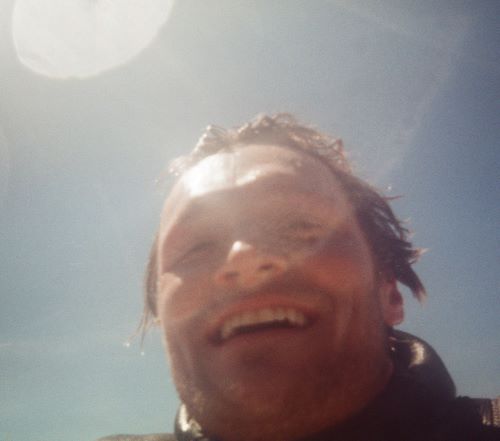 Photo of me up-close from the surface of the water, with sun glint in the background and film grain.